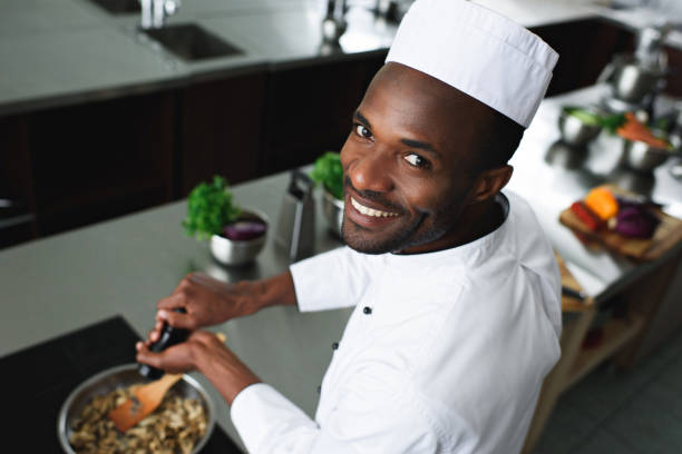 Smiling African american cook seasoning dish by kitchen stove